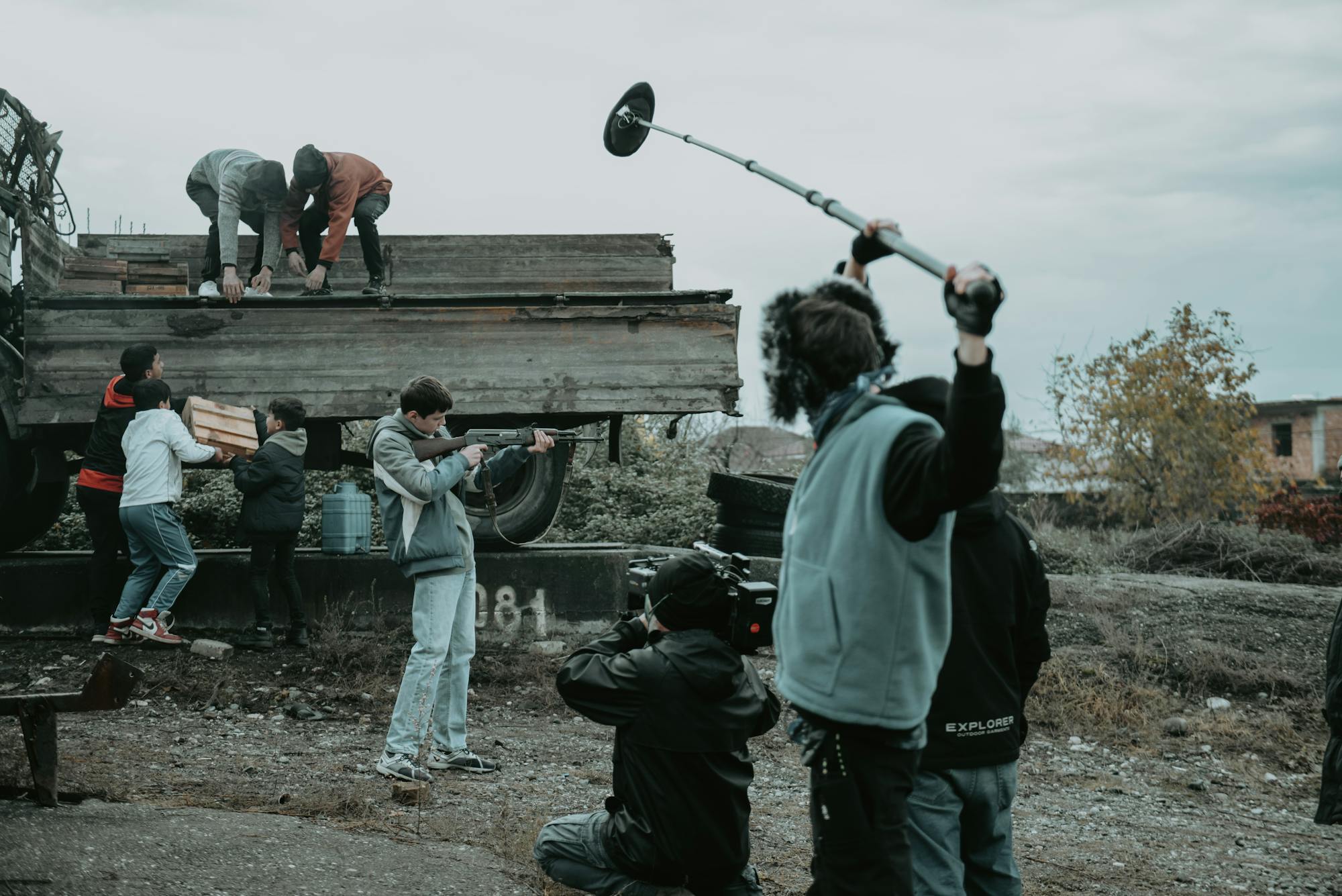 Film crew on an outdoor production set with camera, boom mic and lighting rig